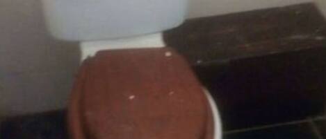 A toilet with a brown seat and lid, white tank, and black floor tiles.