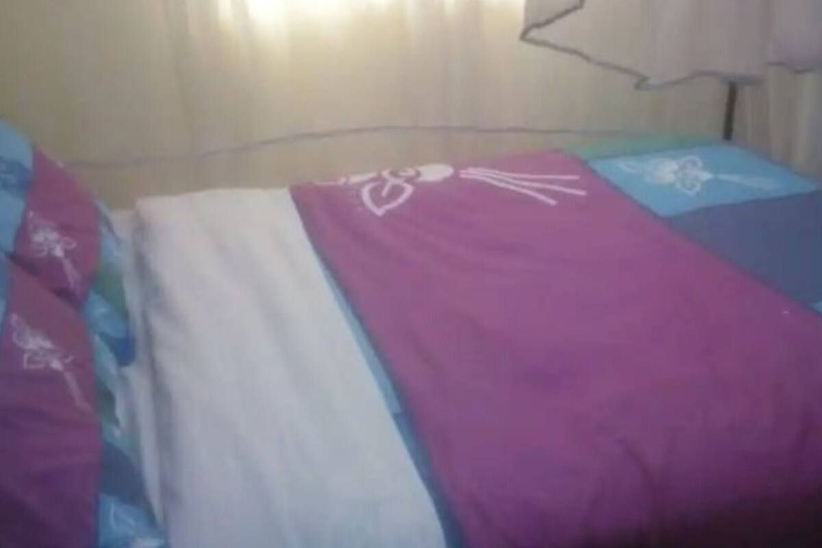 Ein Bett mit einer violett-weißen Tagesdecke und einem blau-weißen Kopfkissen.