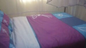 Un lit avec une couvre-lit aux motifs violets et blancs et un oreiller aux motifs bleus et blancs.