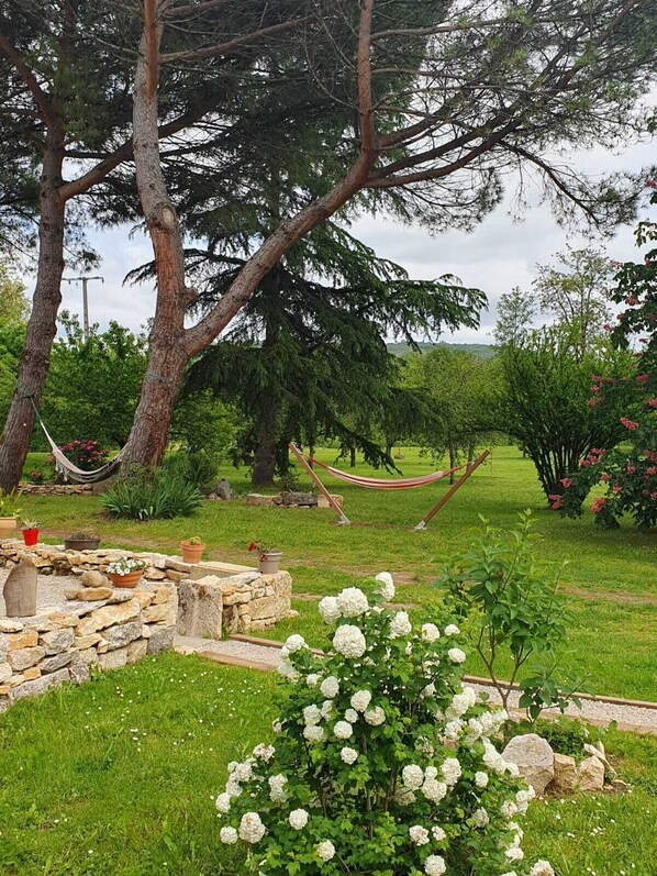 Ein Garten mit Steinmauer, weißen Blumen und einer Hängematte.