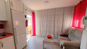 A compact living space with a kitchenette, a sofa, a small table, and a patterned curtain. - Holiday Studio 'Lola' with Mountain View, Private Terrace, A/C & Wi-Fi (Nerja)