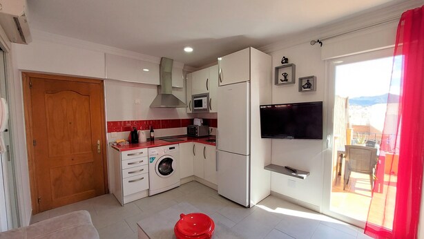 A compact kitchen with a washing machine, microwave, and a TV on the wall. - Holiday Studio 'Lola' with Mountain View, Private Terrace, A/C & Wi-Fi (Nerja)