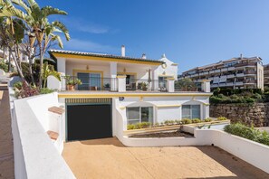 A two-story building with a balcony, a garage, and a landscaped garden area.