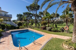 A swimming pool with a tiled deck, surrounded by palm trees and a well-maintained lawn.