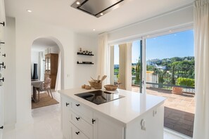 Une cuisine moderne dotée d’un grand îlot central, de meubles blancs et offrant une vue sur la ville grâce à de grandes fenêtres.
