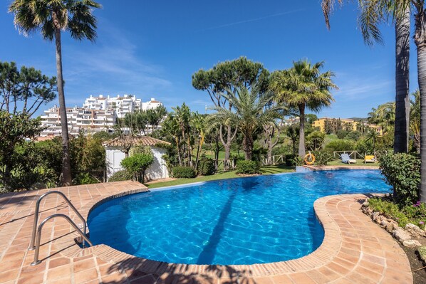 A swimming pool with a curved edge, surrounded by palm trees and a view of residential buildings.