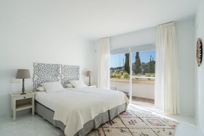 A bedroom with a bed, two bedside tables, a window with curtains, and a view of the outdoors.