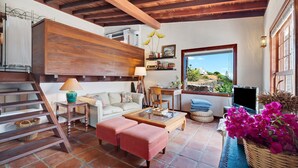 Una sala de estar con techo de madera, una escalera, un sofá, una mesa de centro y un televisor.