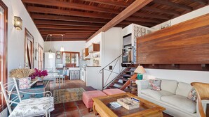Un salón amplio con techo de madera, un sofá, una mesa de centro y una escalera que conduce a un nivel superior.