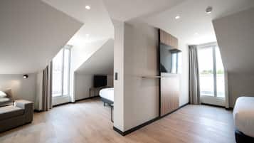 Una habitación de hotel moderna con techo inclinado, un televisor de pantalla plana en la pared, una cama, un sofá y un escritorio.