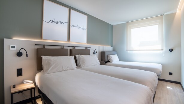 A hotel room with two beds, a bedside table with a phone, and framed artwork on the wall. - Ibis Styles Santander  (Santander)
