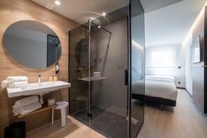 A modern bathroom with a glass-enclosed shower, a large mirror, and a sink with towels. - Ibis Styles Santander  (Santander)