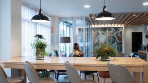 A modern dining area with a long wooden table, six grey upholstered chairs, and two black pendant lights. - Ibis Styles Santander  (Santander)