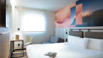 Une chambre d’hôtel moderne avec un grand lit, un bureau avec un ordinateur portable, une chaise et un grand tableau abstrait accroché au mur.