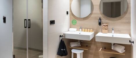 Un baño moderno con dos lavamanos, una cabina de ducha de cristal y un taburete pequeño.
