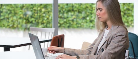 A person working on a laptop at a table with a smartphone beside it.