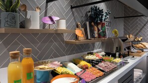 A buffet with various food items, including meats, cheeses, and fruits. There are also bottles of beverages and a bowl of soup. - Ibis Styles Santander  (Santander)