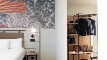 Habitación de hotel con cama, mesita de noche, decoración en la pared y un perchero con bolsas.