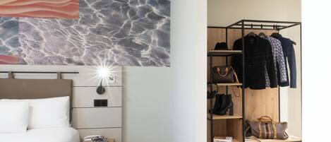 Habitación de hotel con cama, mesita de noche, decoración en la pared y un perchero con bolsas.