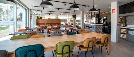 Un café moderno con una mesa de madera larga, sillas coloridas e iluminación colgante.