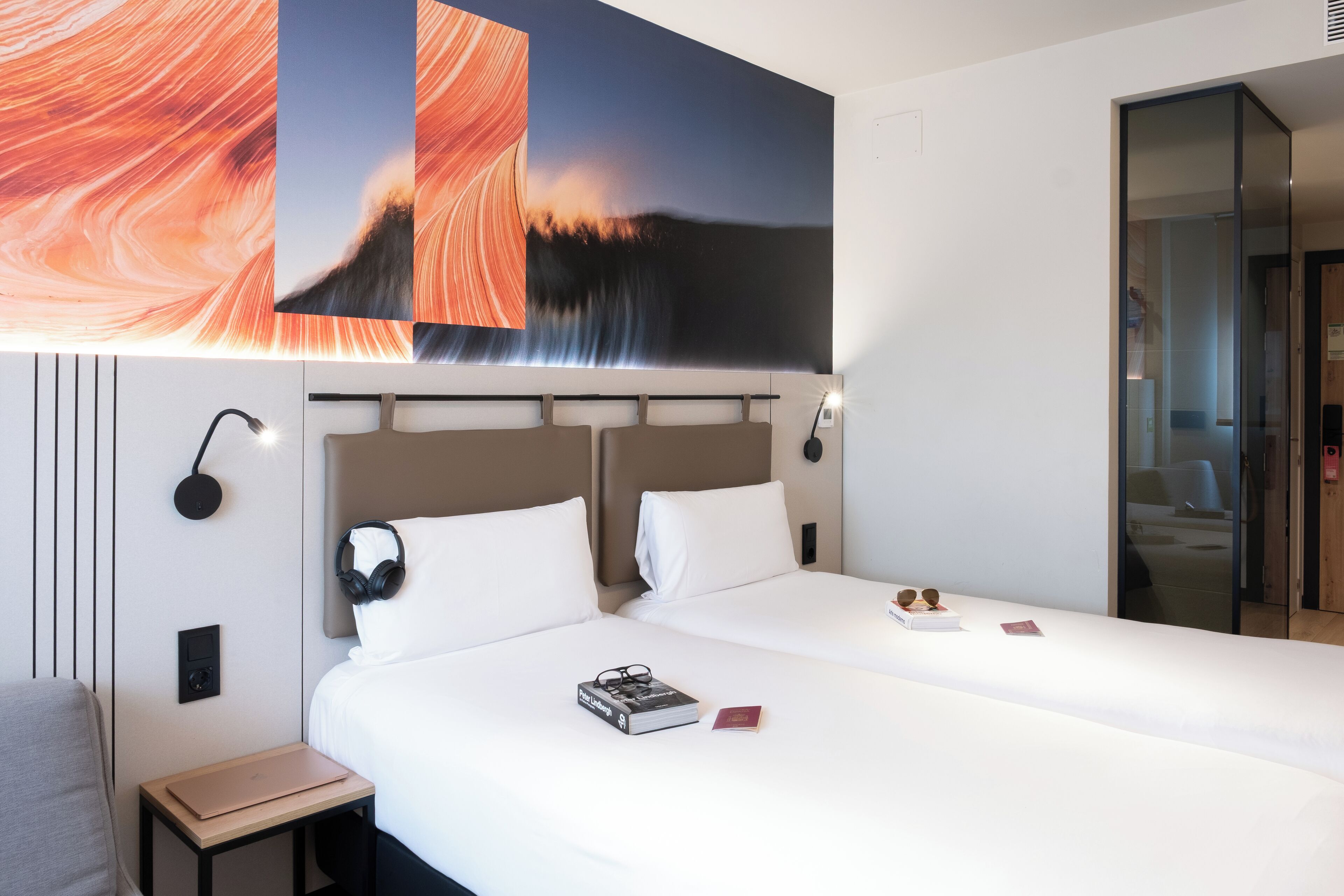 A hotel room with a large bed, a bedside table, a lamp, and a wall-mounted artwork.