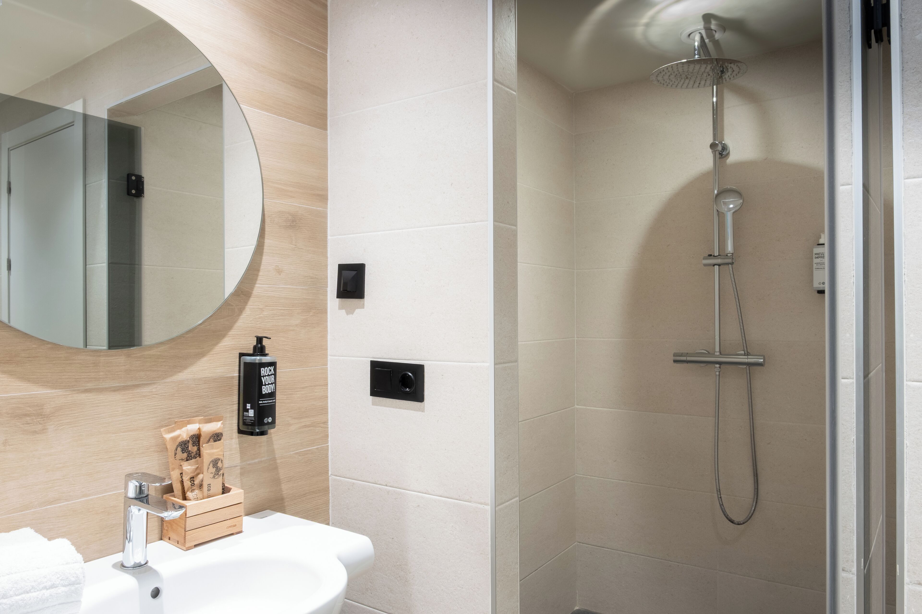 Un baño moderno con un espejo redondo, un lavabo, una ducha y un mueble de tocador de madera.