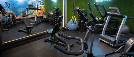 Un gimnasio con diferentes equipos de ejercicio, un espejo grande y un letrero de neón.