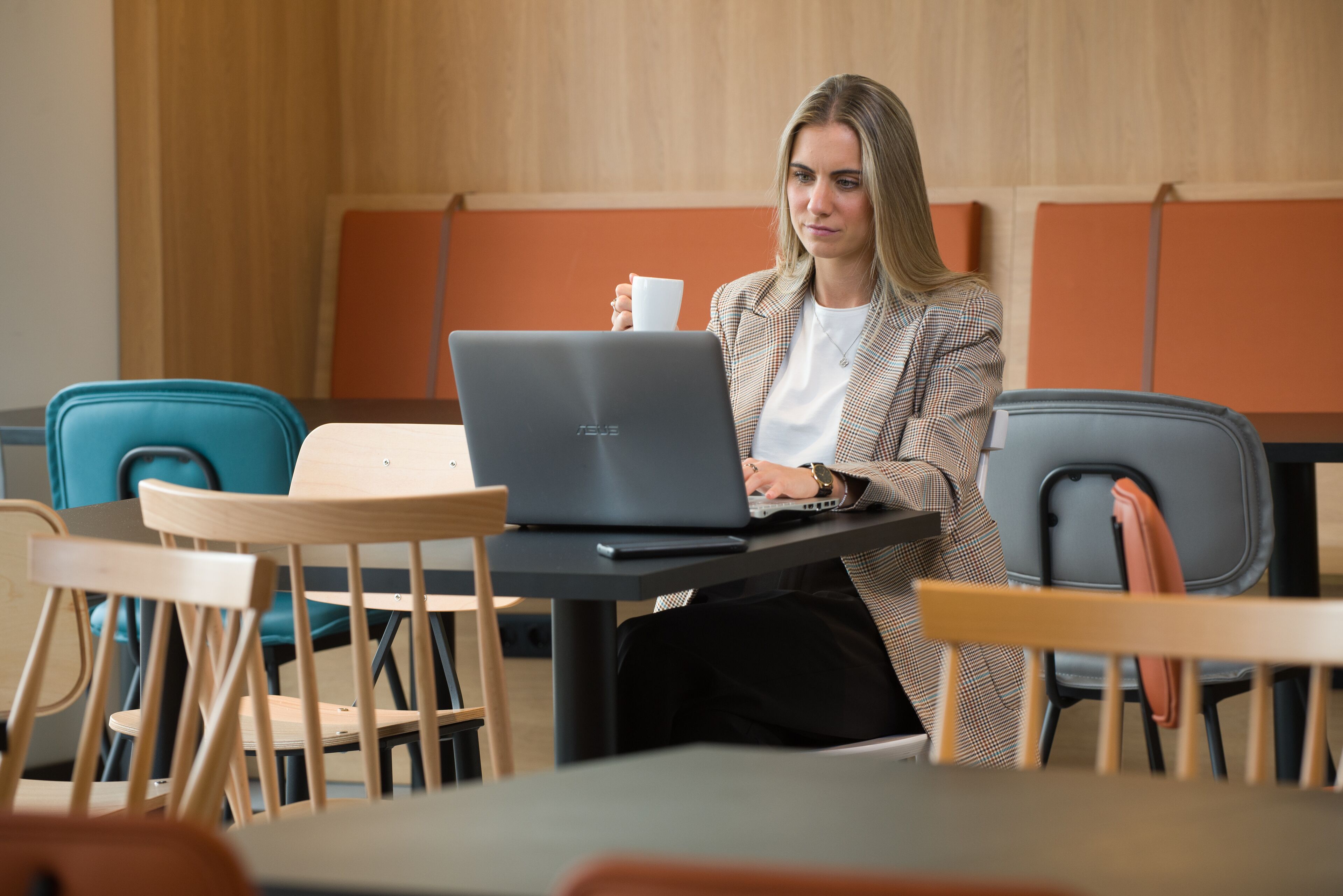 Una persona sentada a una mesa con una computadora portátil, una taza y un teléfono inteligente.