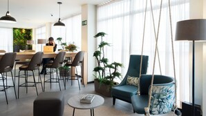 A modern living room with a dining area, a swing chair, and a large potted plant. - Ibis Styles Santander  (Santander)