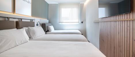 A hotel room with two beds, a television, and a window with blinds.