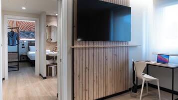 A modern room with a flat-screen TV mounted on a wooden wall, a desk with a laptop, a chair, and a small table with a mirror.