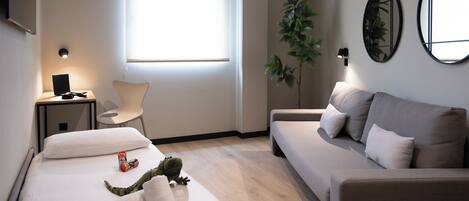 Een moderne hotelkamer met een bed, een bank, een bureau met een lamp, een stoel en een groot raam.