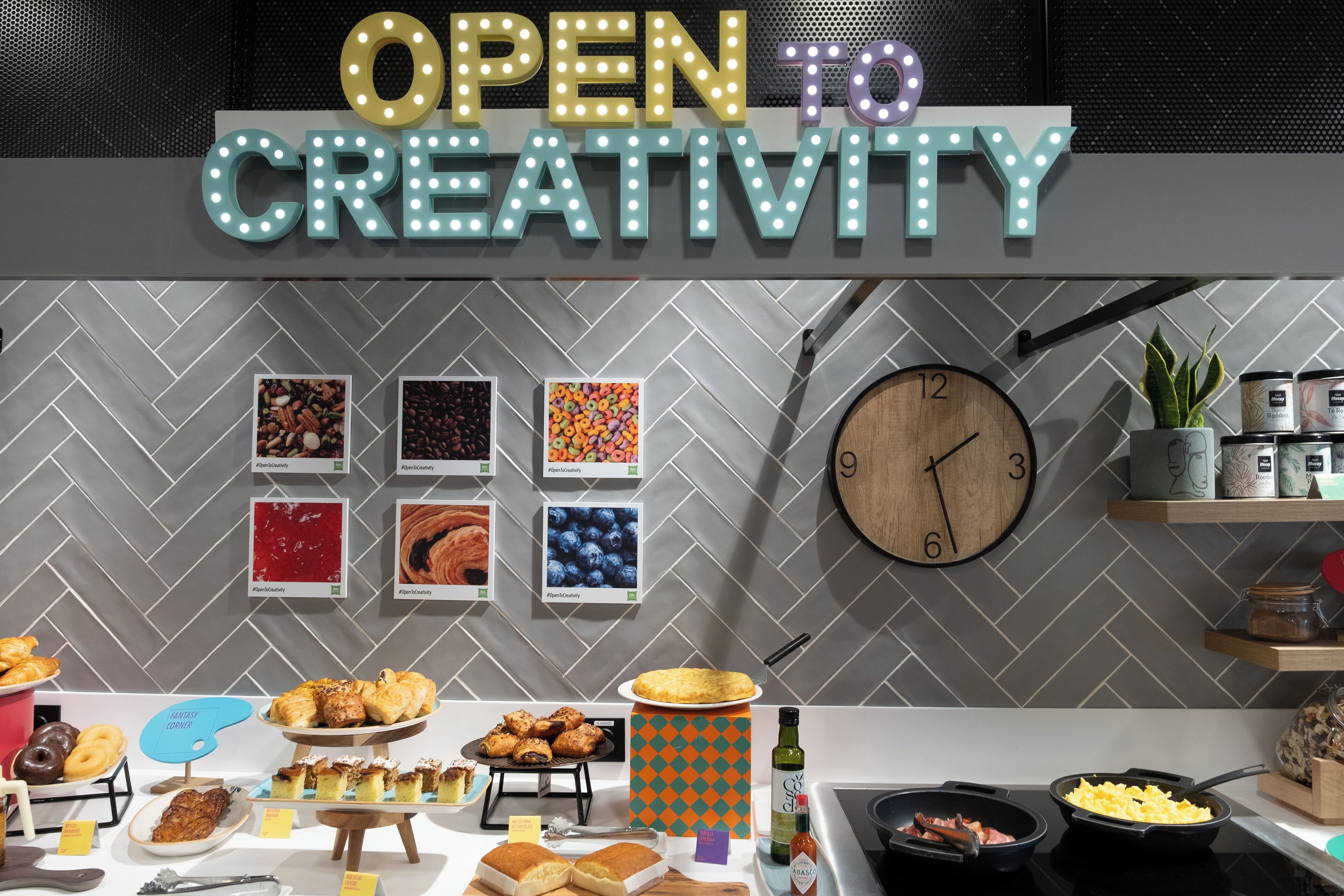 A kitchen area with a clock, various food items, and a sign that reads 'OPEN TO CREATIVITY'.