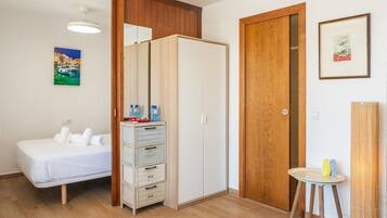 A bedroom with a bed, a wardrobe, a small table with items, a door, and a wall with a picture.