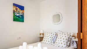 Una habitación de hotel con cama, almohadas, mesita de noche, lámpara, un cuadro y un espejo.