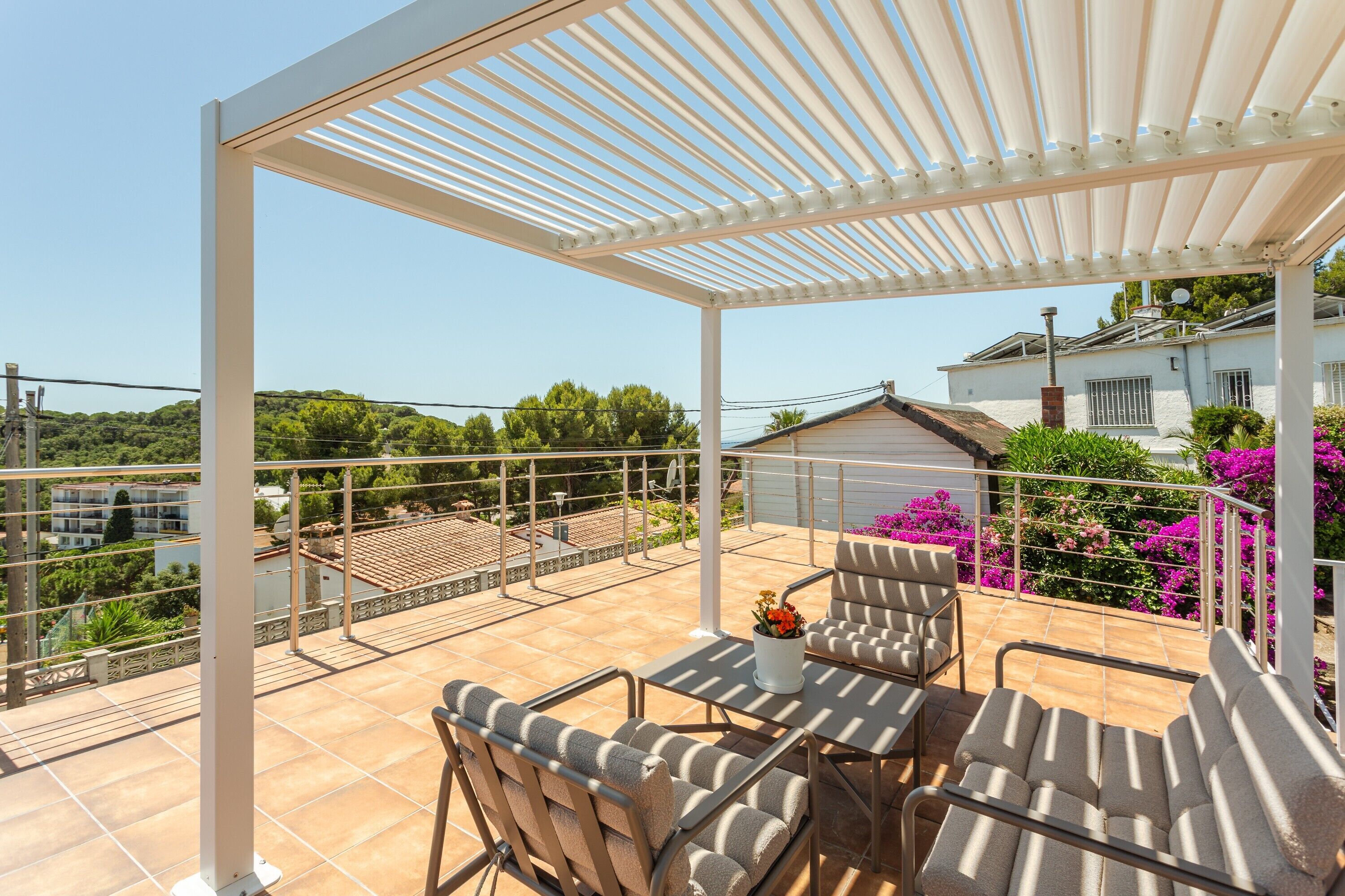Un patio techado al aire libre con una mesa y sillas, vista del entorno y un edificio al fondo.