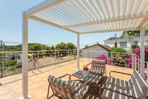 Un patio esterno coperto con tavolo e sedie, vista sulla zona circostante e un edificio sullo sfondo.