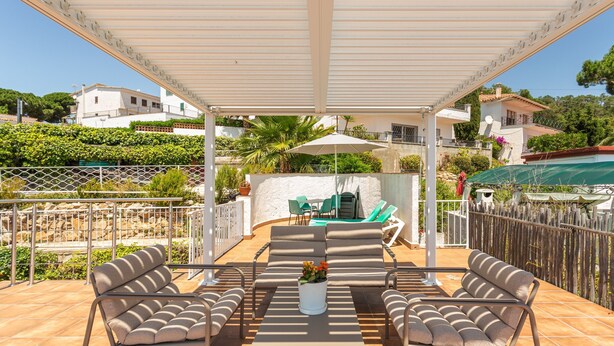 Un patio techado con muebles de exterior, una mesa y una planta en maceta.