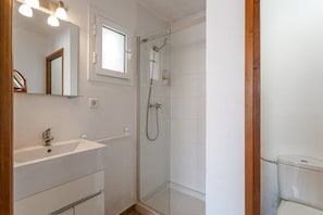 Et badeværelse med en glasafskærmet brusekabine, en hvid vask og et spejl over vasken.