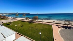 Vista costera con cielo despejado, una playa y un camino que lleva a un edificio de techo plano.
