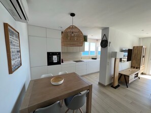 Uma cozinha moderna com armários brancos, forno preto e luminária de vime suspensa.