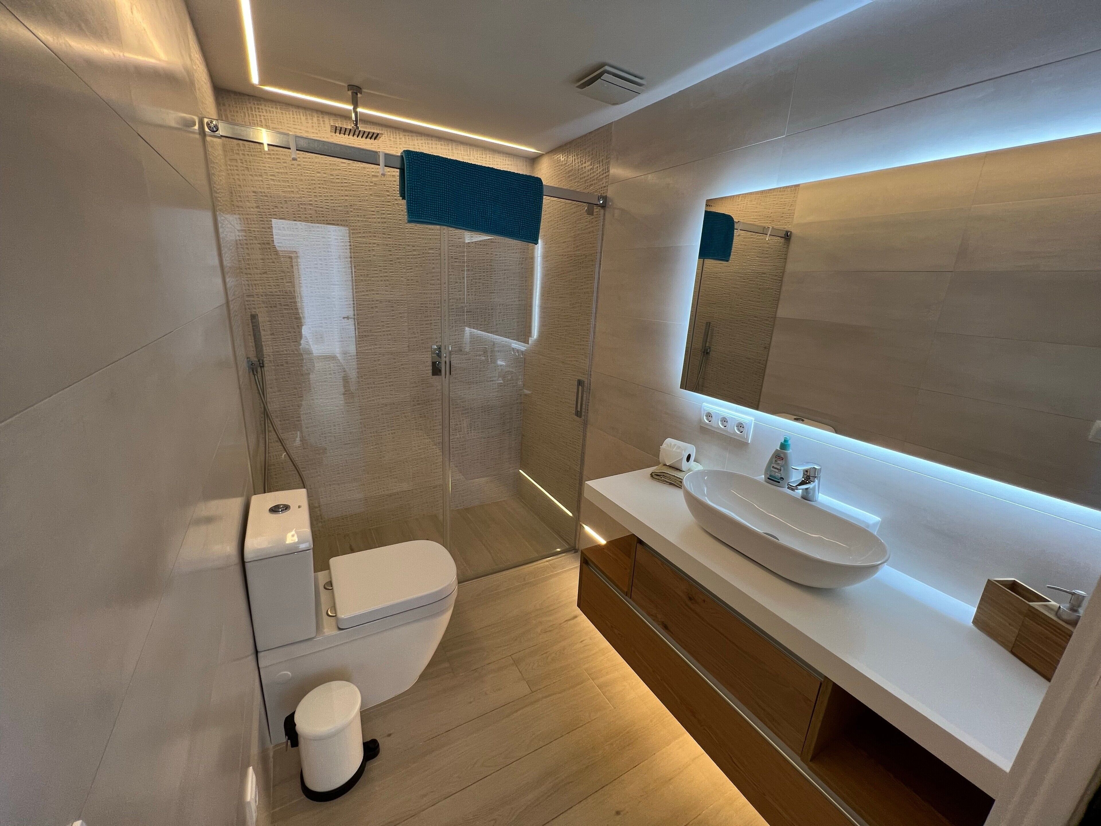 Un baño moderno con cabina de ducha de vidrio, un lavabo blanco y un espejo grande.