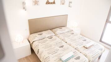 Una cama con cabecera color crema, mesitas de noche blancas y una pared decorada.