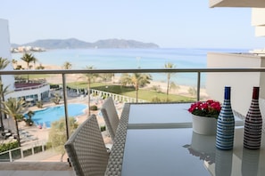 A balcony with a view of the sea, a pool, and a table with two bottles and a flower pot.