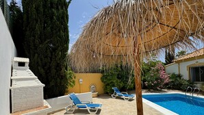 A pool area with lounge chairs, a barbecue grill, and a thatched umbrella.