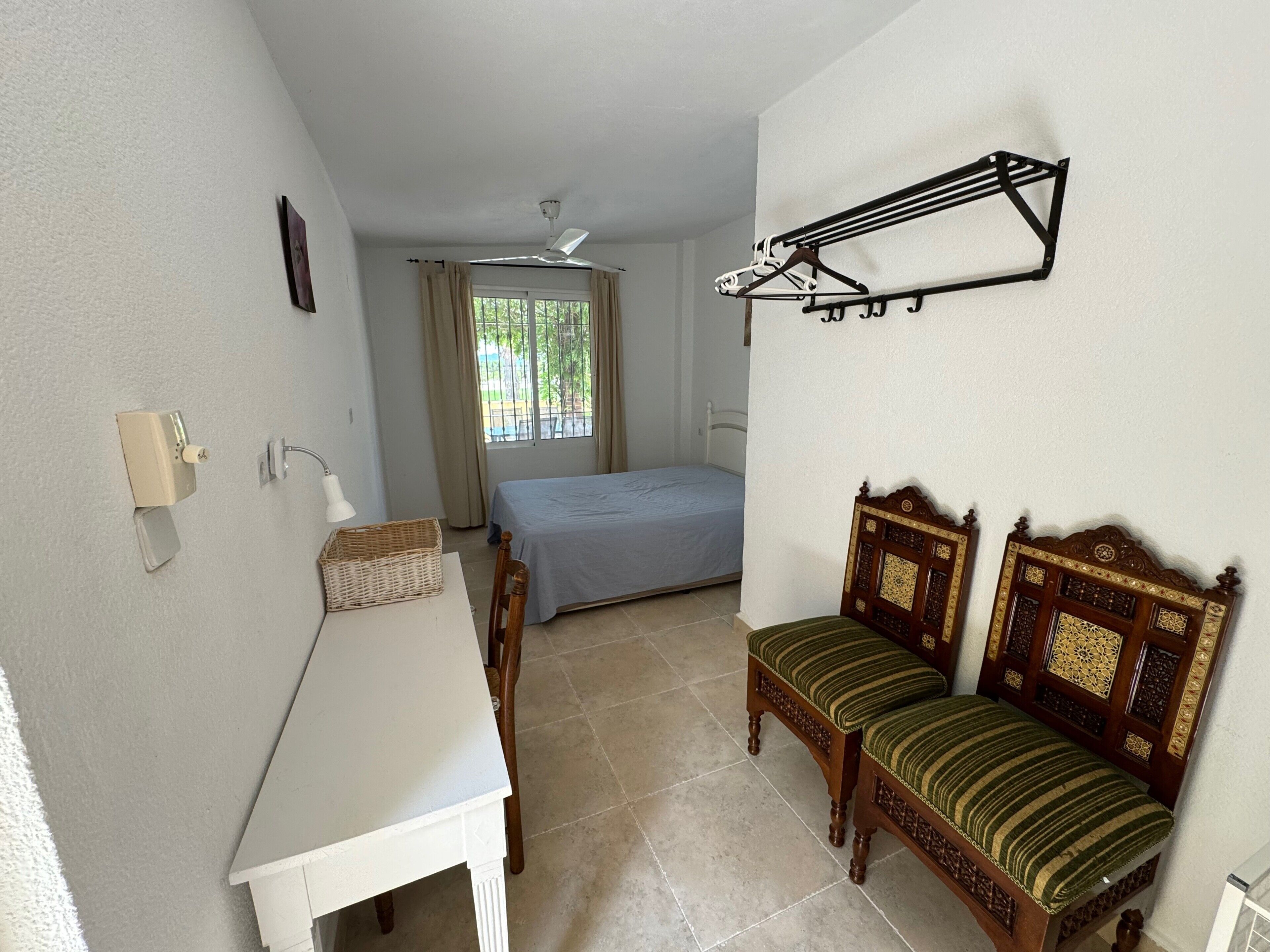Habitació amb llit, escriptori, cadira, penjador de roba i finestra amb cortines.