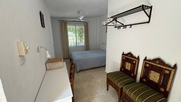Habitació amb llit, escriptori, cadira, penjador de roba i finestra amb cortines.