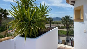 A white building with a balcony, a potted plant, and a view of a mountainous landscape.