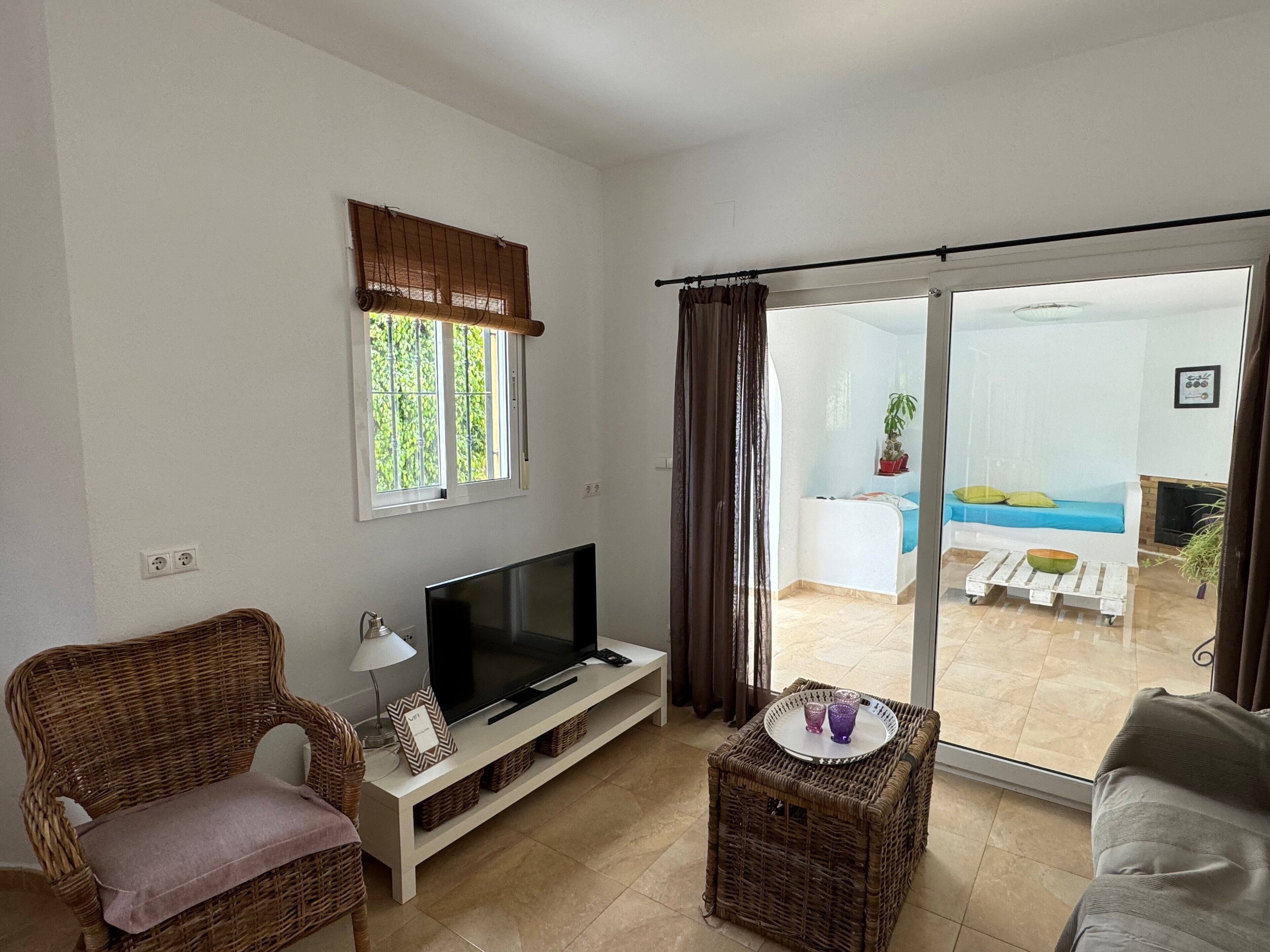 Una sala de estar con televisión, mobiliario de mimbre, una puerta corrediza de vidrio a un balcón y una ventana con vistas.