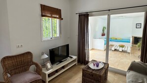 A living room with a TV, wicker furniture, a sliding glass door to a balcony, and a window with a view.